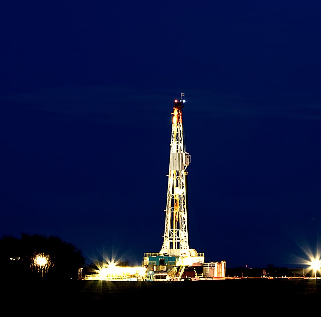 A lit land drilling rig at night on the open plains